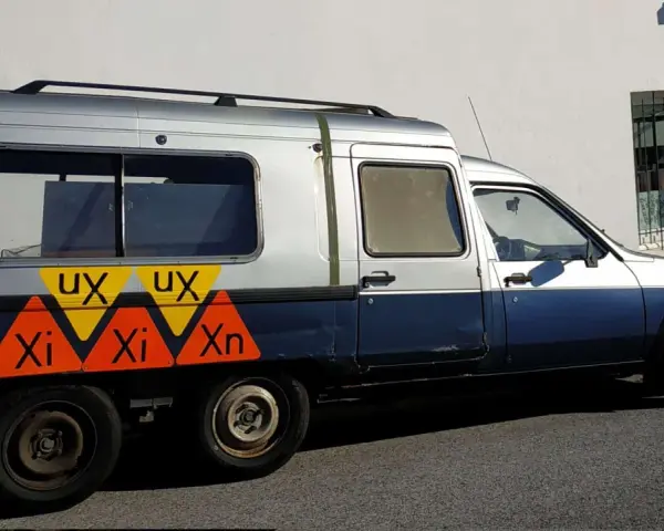 Dwukolorowy Citroen C15 z nietypowymi oznaczeniami "UX" i "Xi Xn" na boku, zaparkowany przy białej ścianie.
