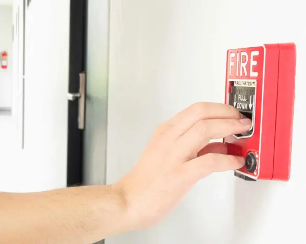 Mano activando la alarma de incendios. Instrucciones claras: "PULL DOWN" para saber cómo apagar alarma de incendios.
