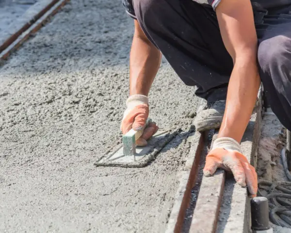 Pracownik wygładza świeży beton, dbając o odpowiednie suchy beton proporcje. Ręce w rękawiczkach trzymają kielnię.