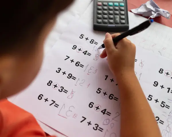 Dziecko rozwiązuje zadania matematyczne, próbując pokonać dyskalkulię. Widoczny kalkulator i zeszyt sugerują naukę.