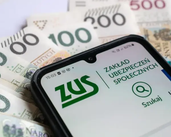 Zasiłek macierzyński 80 czy 100% i 60%? Telefon z aplikacją ZUS na tle polskich banknotów.