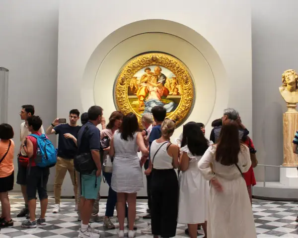 Galeria Uffizi: co zobaczyć? Grupa turystów podziwia okrągły obraz w złotej ramie i rzeźbę.