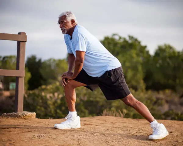 Un homme âgé s'étire pour muscler ses cuisses, un exercice simple en extérieur.