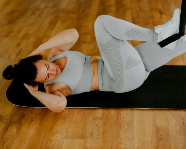 Kvinna gör situps på en matta, med fötterna fästa i ett träningsband. Hon jobbar hårt för att få bort magen på 2 veckor.