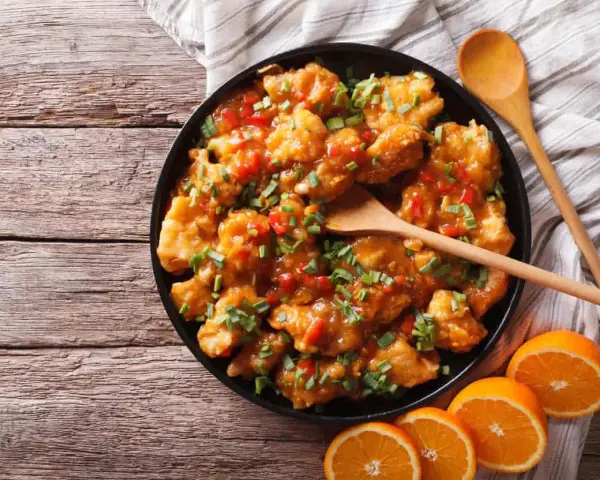 Sabroso pollo a la naranja, cubierto con salsa brillante y cebollín picado, servido con rodajas de naranja fresca.