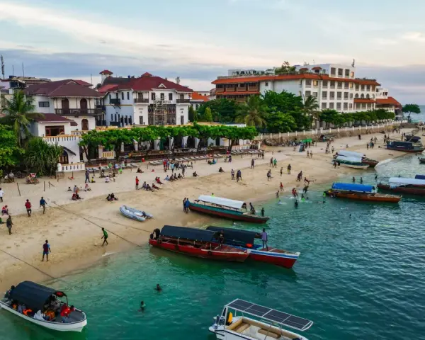 Tanzański szyling na plaży w Stone Town, Zanzibarze. Ludzie odpoczywają, bawią się i pływają, a łodzie czekają na turystów.