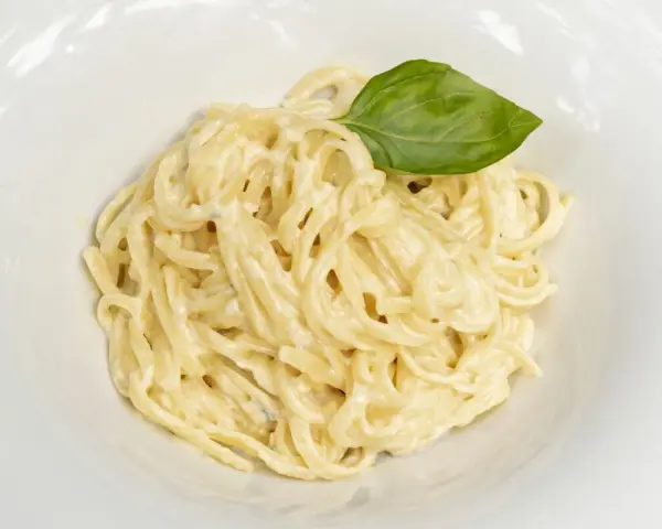 Un plato de spaghetti a la carbonara con nata, cremoso y adornado con una hoja de albahaca fresca.