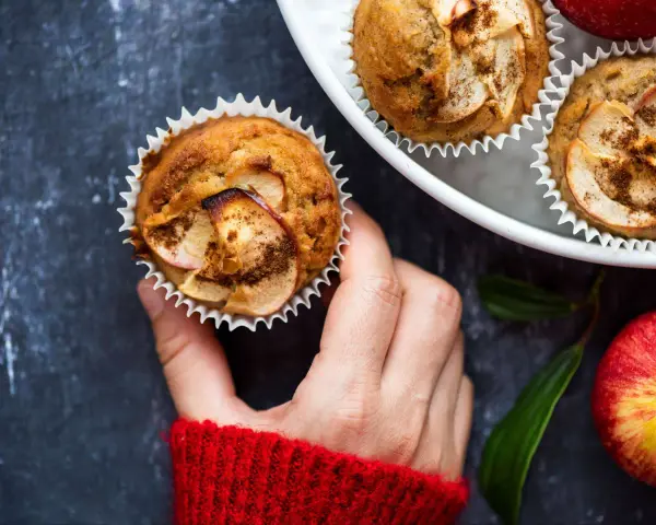 Hand hält einen frisch gebackenen Apfelmuffin, bestreut mit Zimt. Ein tolles Apfelmuffins Rezept!