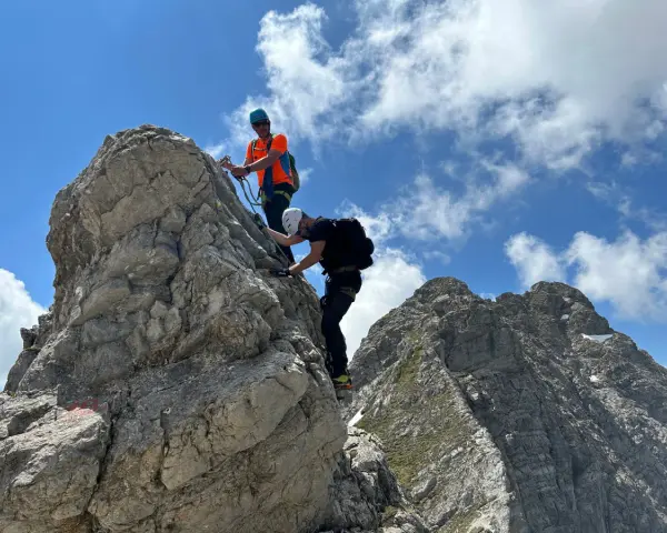 Zwei Bergsteiger meistern den **Hindelanger Klettersteig** auf felsigem Grat unter blauem Himmel mit Wolken.
