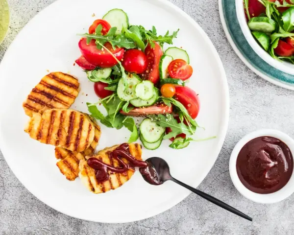 Grillowany ser halloumi z sosem barbecue i świeżą sałatką z pomidorów i ogórków. Idealny pomysł na lekki obiad.