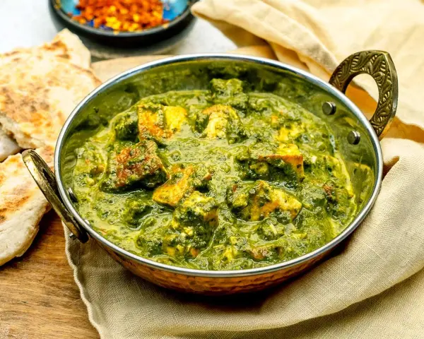 Ein köstliches Palak Paneer in einer Kupferschale, serviert mit Fladenbrot und Chiliflocken.