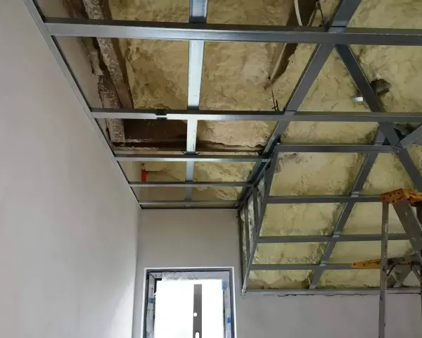 Konstrukcja podwieszanego sufitu z metalowymi profilami i pianką izolacyjną. Widać fragmenty ścian i okna.