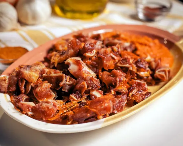 Oreja de cerdo crujiente y dorada servida en un plato con puré naranja.