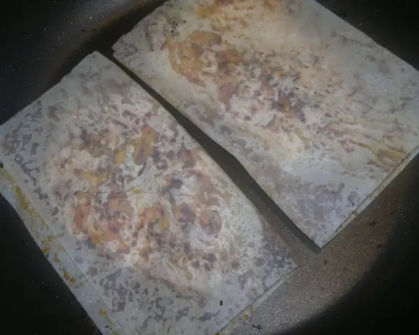 Dwa arkusze papieru ryżowego, przypominające papirus winiary, smażą się na patelni, tworząc chrupiącą przekąskę.