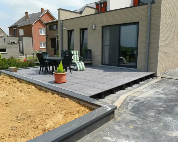 Une terrasse moderne en cours de création, avec des dalles grises surélevées par des plots. Un espace extérieur prêt à être aménagé.