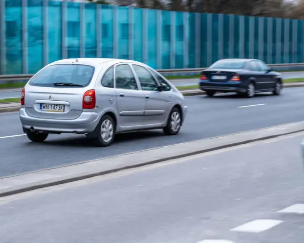 Srebrny Citroën Xsara Picasso jedzie po drodze, mijając inne samochody.