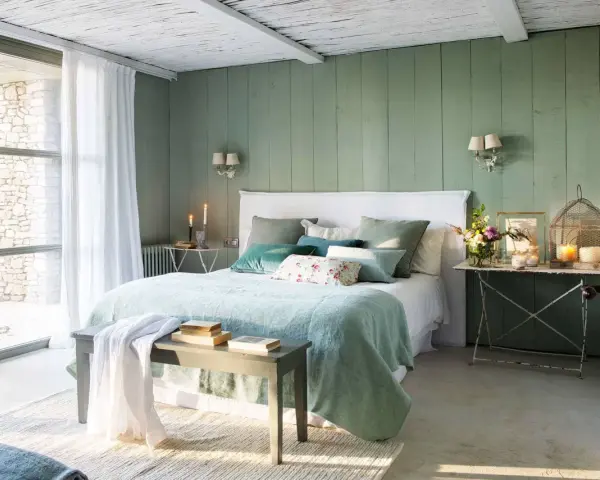 Acogedor dormitorio verde agua y blanco con cama mullida, cojines y luz natural.