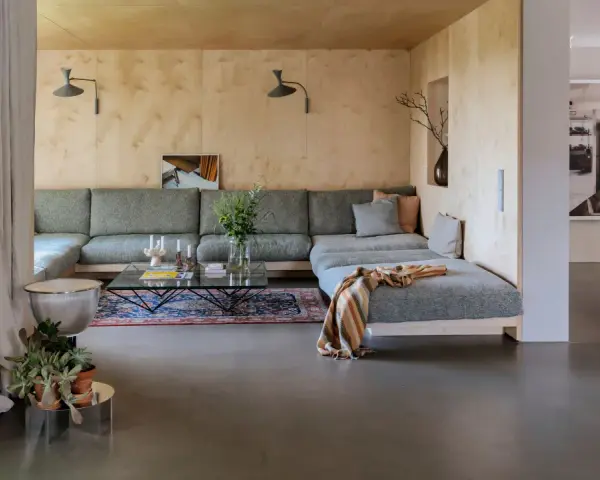 Sofá modular gris, alfombra oriental, mesa de centro de cristal y detalles de interiorismo años 60.