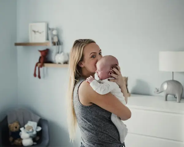 Mama tuli tulula noworodka, kołysząc go czule. W tle pokój dziecięcy z pluszakami.