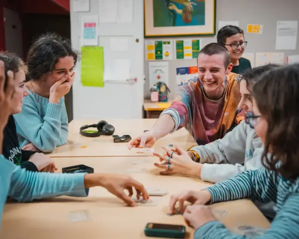Des jeunes rient en jouant à un jeu de cartes autour d'une table.