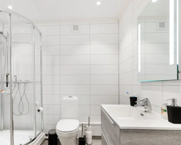 Baño moderno con ducha, inodoro y lavabo. La ventilación del baño es discreta en la pared, asegurando un ambiente fresco.