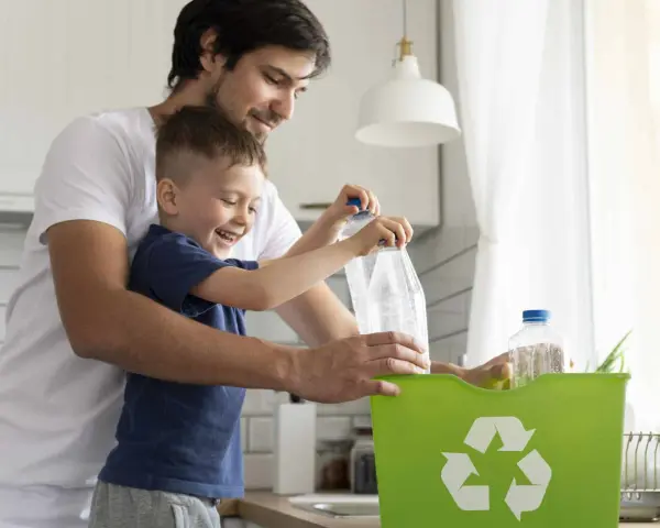 Padre e hijo reciclando botellas de plástico en un contenedor verde. Enseñando conciencia ecológica desde pequeños.