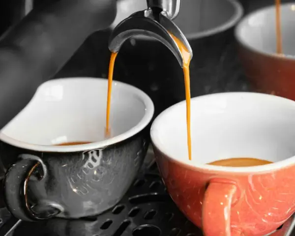 Dwie filiżanki, jedna szara, druga pomarańczowa, napełniają się aromatyczną kawą doppio.