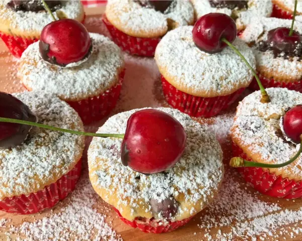 Saftige kirsch muffins, bestäubt mit Puderzucker und garniert mit frischen Kirschen. Ein süßer Genuss!