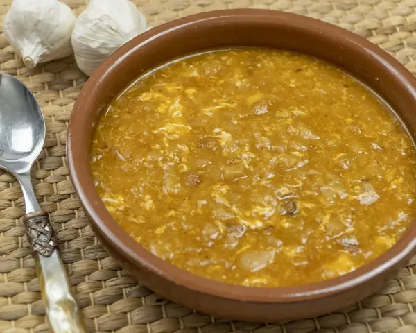 Sopa de ajo tradicional en cuenco de barro, con ajos y cuchara al lado.