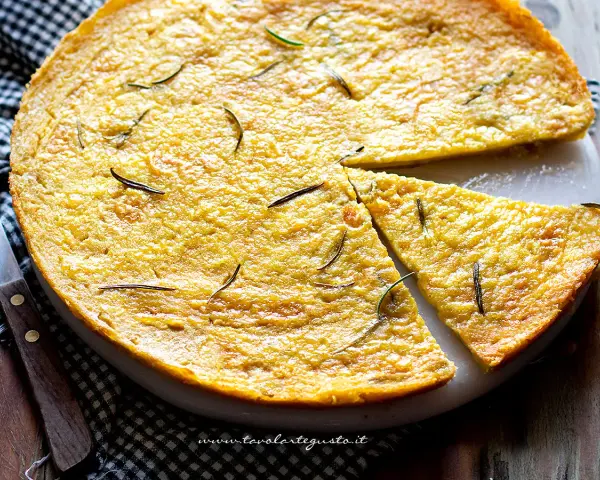 Una torta dorata, profumata al rosmarino, perfetta come ricetta con farina di ceci. Una fetta è già stata tagliata.
