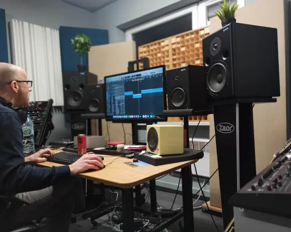 Producent muzyczny pracuje nad miksem i masteringiem w domowym studio. Na ekranie widać sekwencer, a wokół monitory studyjne.