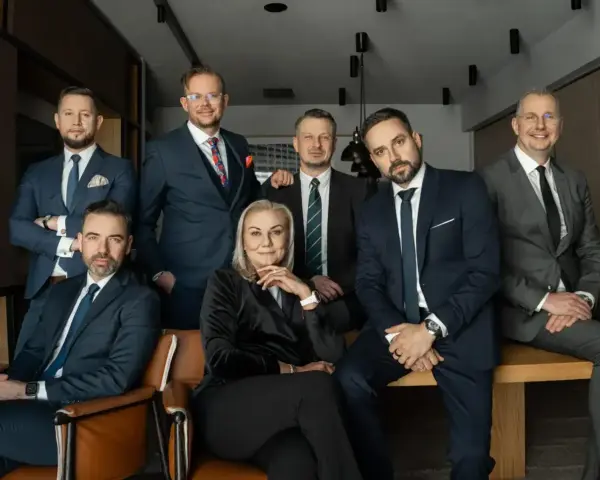 Grupa profesjonalistów w garniturach, w tym jedna kobieta, pozuje do zdjęcia.
