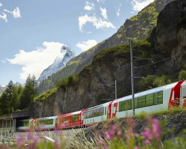 A red and white Glacier Express train travels through the Swiss Alps, with the Matterhorn in the background, on its scenic journey from Zermatt to Andermatt.