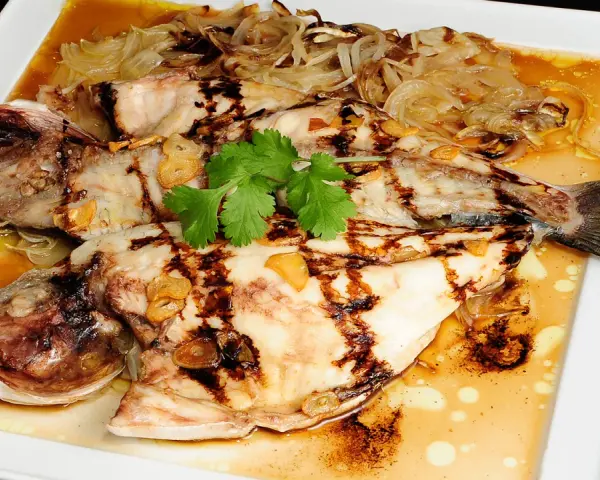 Dorada a la espalda, a la parrilla, con láminas de ajo y cebolla caramelizada, servida en salsa dorada.