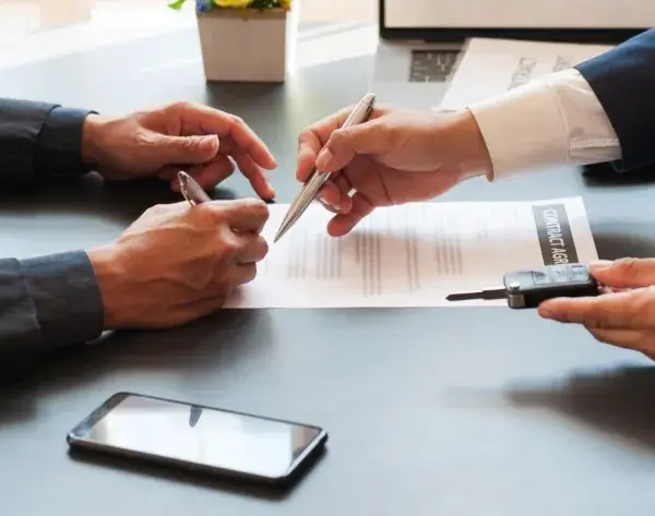 Deux hommes signent un contrat, l'un remettant les clés d'un véhicule. Une transaction pour un **gapd bail commercial** est en cours.