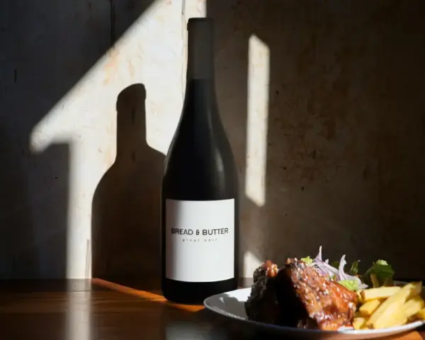 En flaska Bread & Butter Pinot Noir står bredvid en tallrik med revbensspjäll och pommes frites. Perfekt för en mysig kväll.