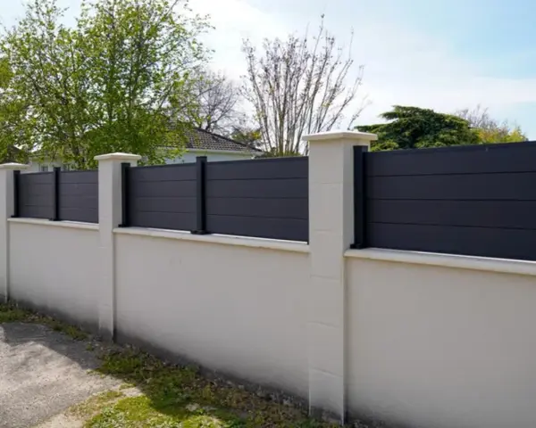 Un mur privatif moderne en composite gris, surmonté de poteaux en pierre, assure l'intimité. Distance à respecter pour une belle clôture.