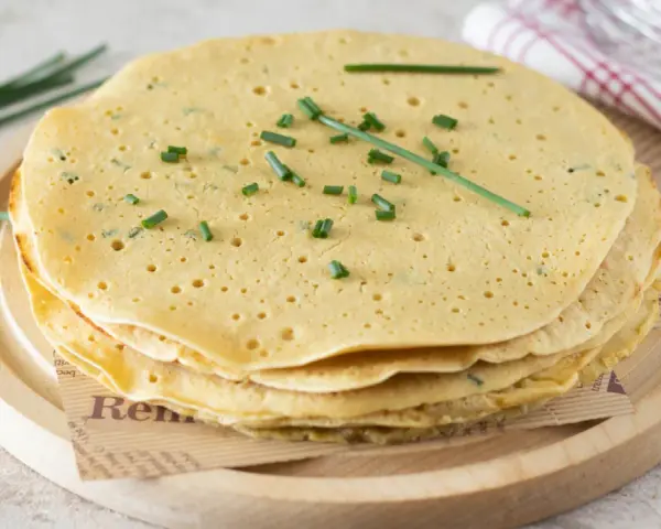 Pila di piadine di ceci dorate, guarnite con erba cipollina fresca. Perfette per un pasto leggero e gustoso.