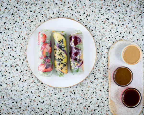 Trzy świeże spring rolls z owocami i warzywami, podane z sosami.