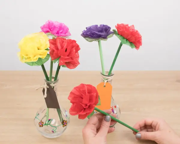 Flores de colores hechas con manualidades de papel de seda, en jarrones decorados.