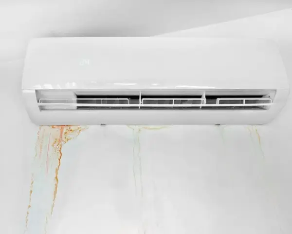 Condizionatore bianco con macchie d'acqua sul muro. La condensa gocciola, creando aloni color ruggine e verdognoli.