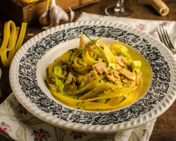 Makaron tagliatelle w kremowym sosie curry z kurczakiem i porem, ozdobiony szczypiorkiem.
