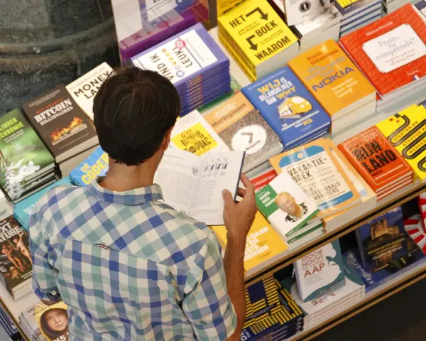 Hombre en una librería, rodeado de libros sobre finanzas y negocios, buscando las mejores editoriales para publicar un libro.