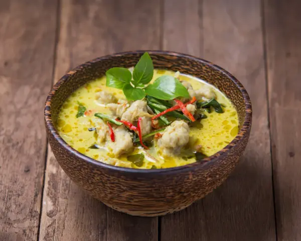 Zielone curry z kurczakiem i chili w drewnianej misce na desce.
