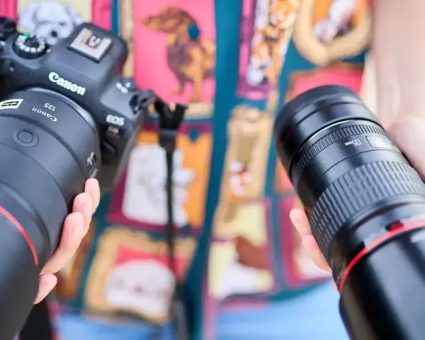 Dwie ręce trzymają obiektywy do Canona. Jeden z nich to Canon RF 135mm f/1.8L IS USM, drugi to Canon EF 135mm f/2L USM.