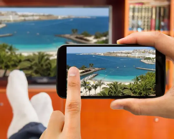 Jak podłączyć telefon do telewizora przez HDMI? Widok na plażę z palemami na ekranie telefonu i telewizora.