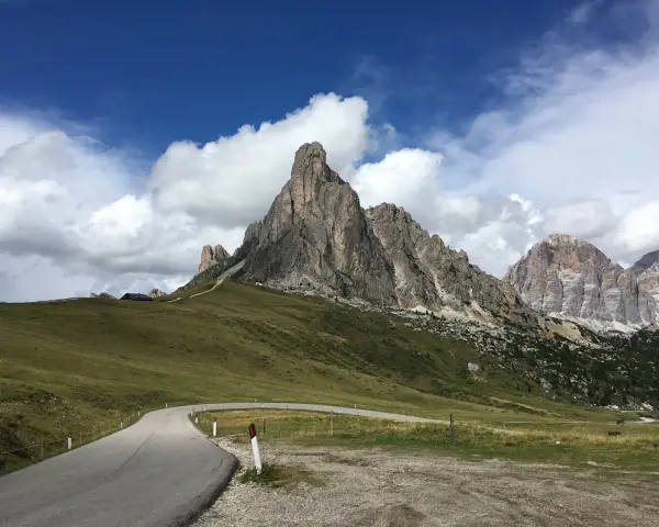Strada tortuosa verso le Dolomiti, perfetta per una gita in moto. Montagne imponenti e cielo azzurro con nuvole bianche.