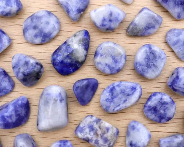 Tumbled sodalite stones, showcasing their deep blue and white patterns. Le pietre di sodalite, con le loro proprietà calmanti, sono disposte su un fondo di legno.