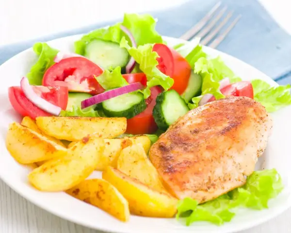 Petto di pollo in friggitrice ad aria, patate arrosto e insalata fresca con pomodori, cetrioli e cipolla rossa.