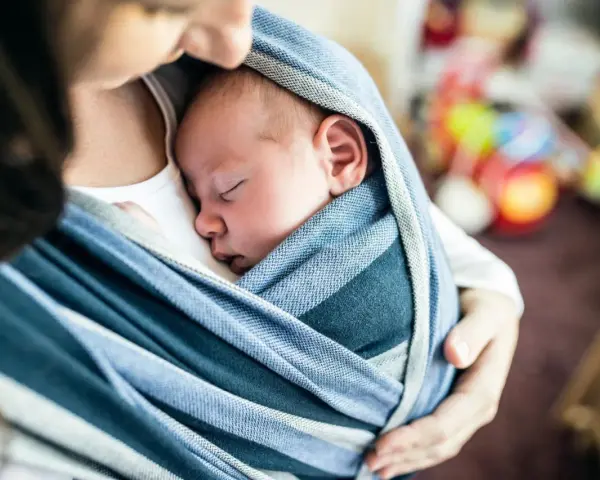 Ein Baby schläft friedlich in einem blauen Tragetuch. Der sanfte Tagesrhythmus des Babys wird durch die Nähe zur Mutter unterstützt.